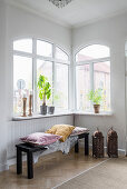 Cushions and fur rug on black bench in corner below windows