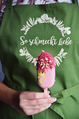 A woman holding a pink ice cream stick with gold leaf