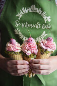 A woman holding three ice cream cones with cherries and pistachio nuts