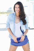 A dark-haired woman wearing a bathing suit, a denim shirt and shorts