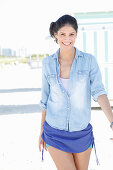 A dark-haired woman wearing a bathing suit, a denim shirt and shorts