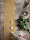 Hands of anonymous cook squeezing creamy filling on thin ravioli dough near bunch of fresh sorrel