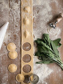 Bunch of ripe sorrel and various utensils placed over flour near uncooked raviolis and dough