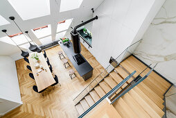 View down onto island counter, dining area and staircase in high-ceilinged room with skylights in sloping wall