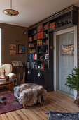 Deckenhoher Bücherschrank aus dunklem Holz davor Antiksofa und Polsterhocker mit Tierfell