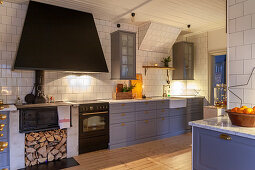 Modern country-house kitchen with blue-grey cupboards, antique wood-fired stove and white-tiled wall