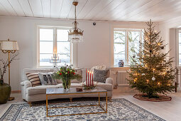 Geschmückter Weihnachtsbaum, helle Couch und Couchtisch im Wohnzimmer