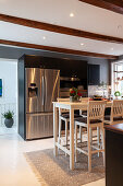 Wooden table and barstools in modern kitchen with wood-beamed ceiling