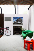 Green designer armchairs and red stacking stools next to an antique fireplace