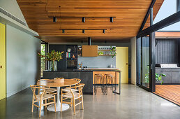 Living room under a pointed wooden roof with an open kitchen and floor-to-ceiling sliding doors to the terrace