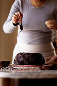 A woman decorating a Gluten-free Chocolate Budnt cake with chocolate drizzle