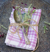 A fabric napkin with a silver spoon and a sprig of thyme