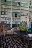 Bottle garden on black coffee table in front of bookcase with mint-green back wall