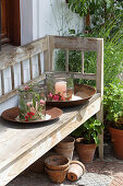 Glass candle lanterns decorated with summer flowers and leaves on wooden bench