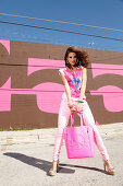 A brunette woman with a shopping bag wearing a pink top and trousers