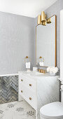 Waschtisch mit Marmorplatte und Messing-Armatur, darüber Spiegel und Wandleuchte, sechseckigen Marmorfliesen auf dem Boden