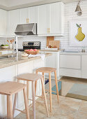 White kitchen with light wood accents, white subway tiles and island counter with light wooden bar stools