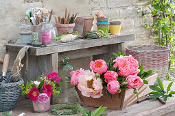 Freshly cut flowers of peony in a wooden box and a small bouquet of roses on the pot table
