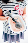 A girl holding peach sorbet with an ice cream scoop