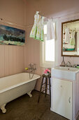 Vintage bathtub, sink on washstand and girl's dresses on clothes line in bathroom