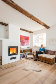 Woman sitting on sofa in bright living room with wooden floor and fireplace