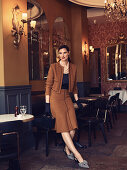 A dark-haired woman in a restaurant wearing an elegant, brown suit