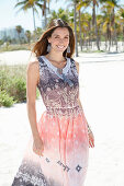 A brunette woman on the beach wearing a light summer dress with an ethnic pattern