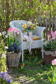 Wicker armchair with a spring bouquet between buckets with spring plants on the garden fence