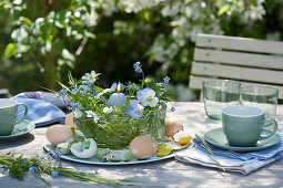 Easter table decoration on the terrace with pansies, grass, Easter eggs, and candle