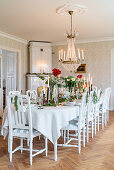 Long, festively set dining table below chandelier in manor house