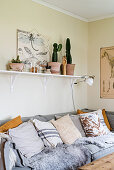 Collection of scatter cushions on pale grey sofa below cacti on shelf