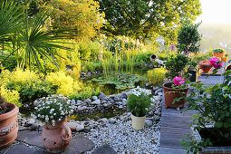 Gartenteich umgeben von Topfblumen auf Steinplatte, Kies und Holzdeck