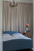 Bed with blue, button-tufted frame in bedroom with wall hanging