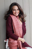A young brunette woman wearing a wine-red cardigan with a salmon pink woollen shawl