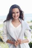 A young brunette woman wearing wearing a white tunic with a woollen jumper over her shoulders