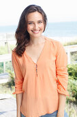 A young brunette woman wearing a salmon-pink tunic blouse