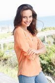 A young brunette woman wearing a salmon-pink tunic blouse and jeans