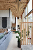 Grey sofa set, partition and houseplant next to glass wall with staircase in background