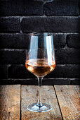 A single glass of rose wine on a rustic wood with black brick background