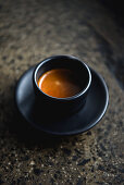 Espresso black coffee in a black cup and saucer on a stone worktop