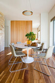 Round table with marble top and pale chairs in dining area with slatted wooden partition in background