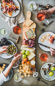 Charcuterie and cheese board, rose wine, nuts, olives and peoples hands holding glasses and food