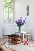 Vase of delphiniums on child's table with bench and stools