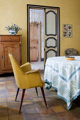 Gelber Polsterstuhl am Tisch im mediterranen Esszimmer mit Terracottafliesenboden