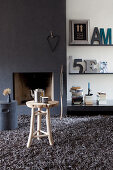 Fireplace in dark chimney breast and decorative letters on shelves in living room with grey long-pile rug