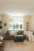 Graues Sofa und Truhe als Couchtisch vorm Erkerfenster im Wohnzimmer