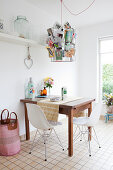 Small wooden breakfast table and classic chairs below metal lampshade decorated with postcards
