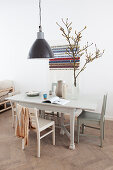 Black pendant lamp above the dining table with chairs, branch in a vase, behind it wall hanging with message