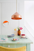 Green-painted kitchen table below copper pendant lamp