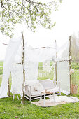 Sofa in the DIY garden pavilion made of branches and a white curtain